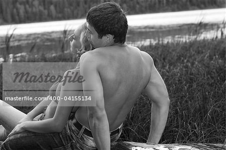 a man and a woman in tender pose sitting on the log (black and white picture)