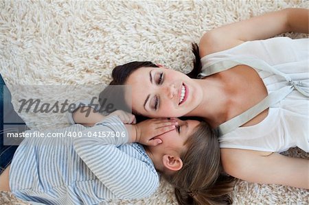 Smiling mother and her daughter lying on the floor with their heads together