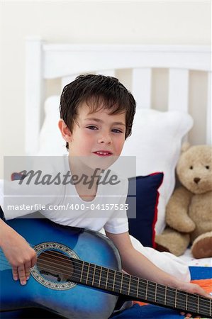 Portrait of a little boy playing guitar on bed