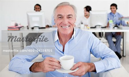 Senior businessman drinking a coffee with his team in the background