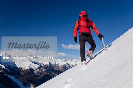 A male climber , dressed in red, climbs down a snowy slope. Winter clear sky day. In background the Monte Rosa massif, Italy, Europe.