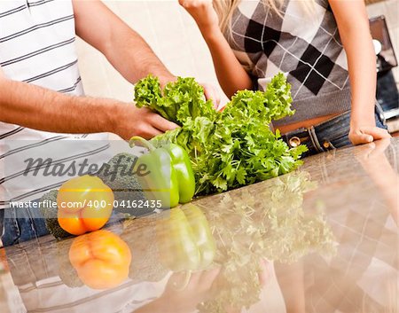 Cropped view of a young couple stand behind a kitchen counter full of vegetables. Horizontal shot.