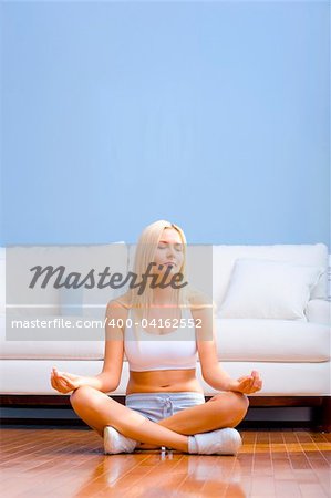 Young woman sitting cross legged on floor with hands on knees meditating. Vertical shot.