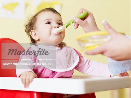 mom giving homogenized food to her daughter on high chair. Horizontal shape