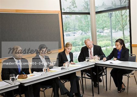 Business people sitting at table in meeting doing paperwork.  Horizontally framed shot.
