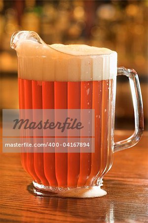 Full beer pitcher with foam on a bar counter. Vertical shot.
