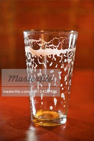 Empty beer glass on bar counter with residual foam lining the glass. Vertical shot.