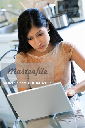 Young woman concentrates on working with a laptop at a glass kitchen table. vertical shot.