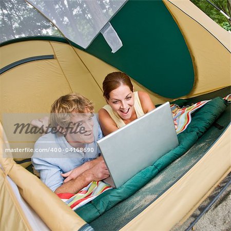 Couple laying in tent using laptop