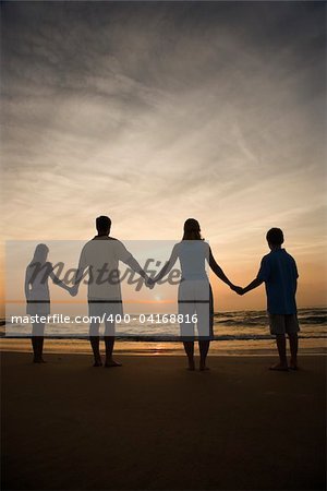 Silhouette of family holding hands on beach watching the sunset. Vertically framed shot.