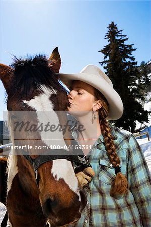 Attractive young woman wearing a cowboy hat and kissing a horse. Vertical shot.