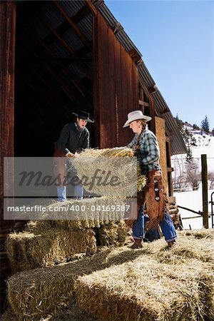 Attractive young man and woman lifting hay bales on a farm in front of a barn. Vertical shot.