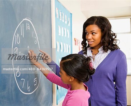 Teacher and female student at the blackboard with clock drawing on it.