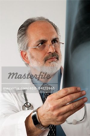 Portrait of a doctor wearing eyeglasses and a white lab coat and looking intently at an x-ray. Vertical shot. Isolated on white.