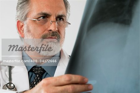 Cropped close-up portrait of a doctor wearing eyeglasses and a white lab coat and looking intently at an x-ray. Horizontal shot. Isolated on white.