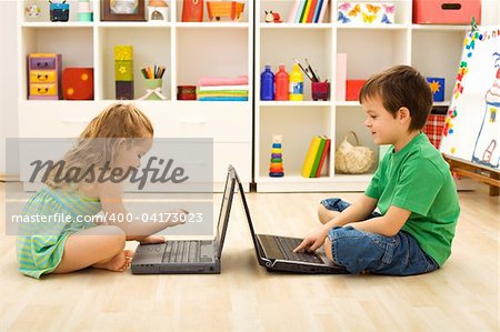 Kids learning and playing computer games sitting on the floor with laptops