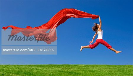 Belle jeune femme sauter dans un pré vert avec un tissu coloré