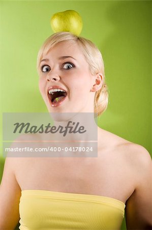 funny shot of a nice girl with a green apple on her head making face