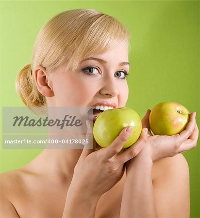 very cute blond girl in act to bite a green apple on colored background