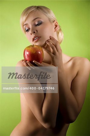 fashion and glamour shot of a dreaming nude young woman with red apple on green background