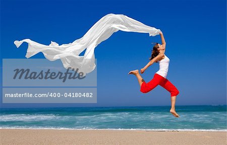 Beautiful young woman jumping on  the beach with a colored tissue