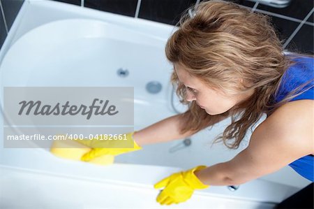 Young woman cleaning a bath with a sponge