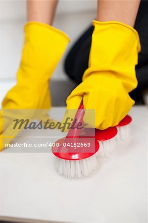 Close-up of a woman cleaning a bathroom's floor with a yellow rubber glove