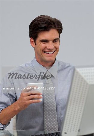 Positive businessman holding a drinking cup sitting at his desk