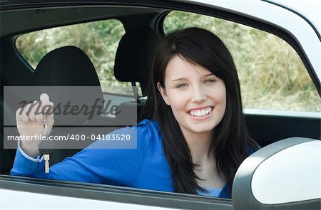 Jolly teen girl sitting in her car holding keys after bying a new car