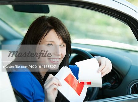 Charming brunette teen girl sitting in her car tearing a L-sign after having her driver's licence