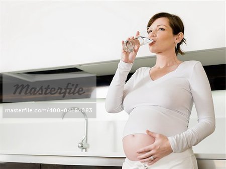 portrait of italian 6 months pregnant woman drinking water in kitchen. Horizontal shape, copy space