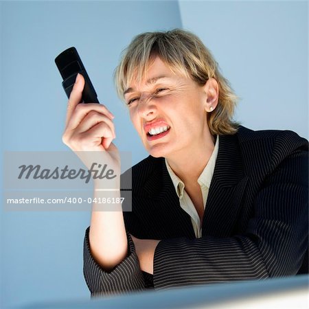 Caucasian businesswoman looking at cellphone and sneering in frustration.