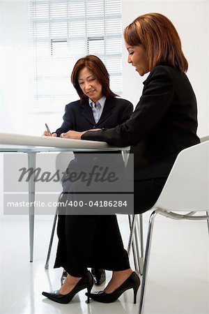 Businesswomen discussing paperwork at office desk smiling.