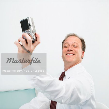 Caucasian middle aged businessman taking picture of himself with camera smiling.