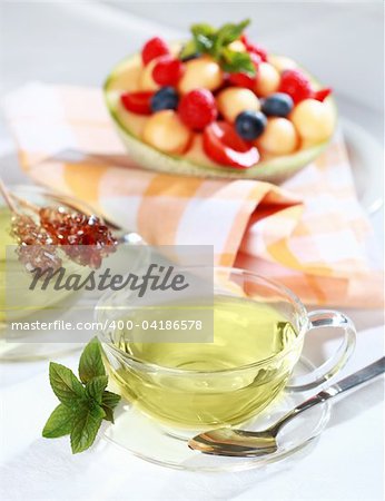 Two cups of green herbal tea with sugar stick and fresh fruits