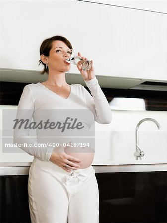 portrait of italian 6 months pregnant woman drinking water in kitchen. Vertical shape, copy space