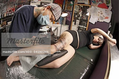 A tattoo artist applying his craft onto the leg of a female. Shot with fisheye lens.