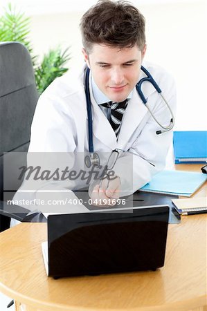 Assertive male doctor using a laptop sitting at his desk in a practice