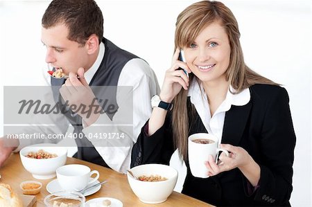 Smiling businesswoman talking on phone while having breakfast with her husband at home