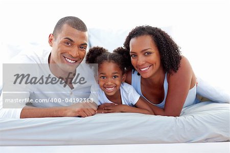 Affectionate parents and their daughter lying on a bed smiling at the camera