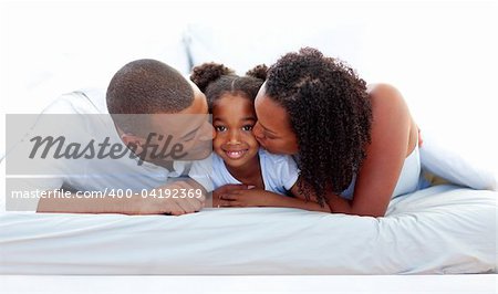 Cheerful parents kissing their daughter lying on a bed