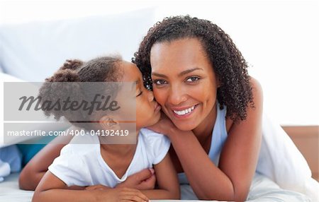 Loving little girl woman kissing her mother lying down on bed at home