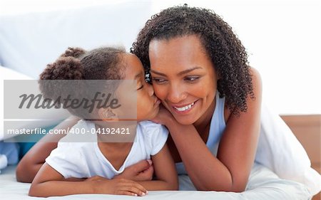 Cute little girl woman kissing her mother lying down on bed at home