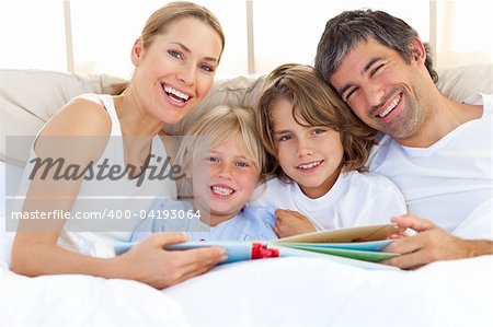 Smiling family reading a book  lying in bed