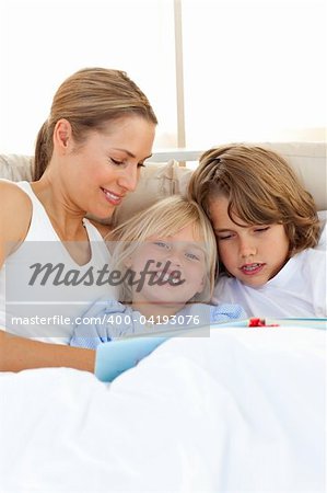 Pretty mother and her children reading book lying in bed