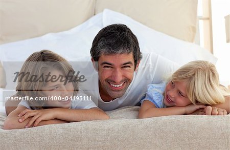 Smiling father talking with his children lying on bed at home
