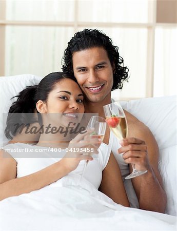 Happy young couple toasting with Champagne lying on the bed