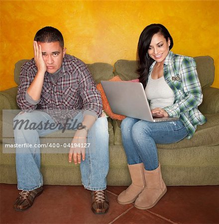 Hispanic Couple on Green Couch with Computer Man is Bored