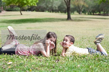 Cute children lie down on green grass and looking eachother in the park, outdoor