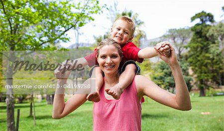 Happy mother giving her son a piggyback ride in a park